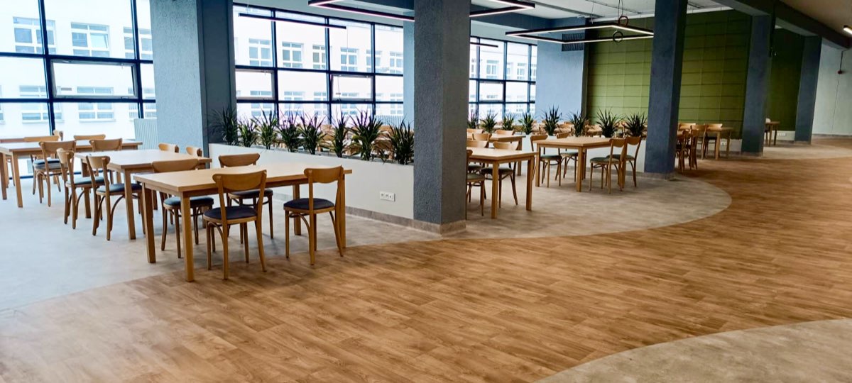 Sala jadalna z drewnianymi stołami, dużymi oknami i parkietem