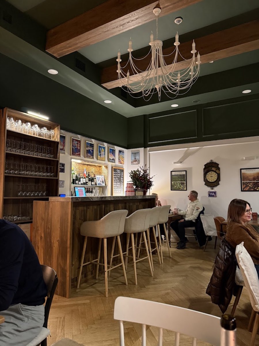 Wnętrze Le Rendez-Vous: zielone ściany, drewniany sufit z belką, biały żyrandol i drewniany bar z kieliszkami